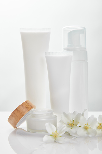 Jázmin virágok fehér felületen, közel a tejszínhez, üveghez és kozmetikai adagolóhoz - Fotó, kép