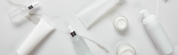 plano panorámico de botellas de vidrio cosmético, frascos con crema, tubos hidratantes y dispensador en la superficie blanca
 - Foto, Imagen