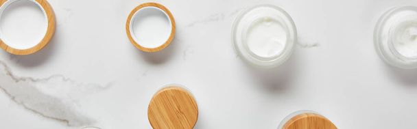 panoramic shot of jars with cosmetic cream and wooden caps on white surface - Photo, Image