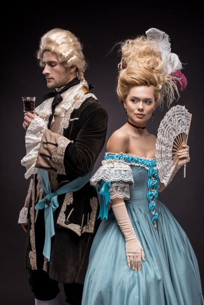 handsome man with wine glass near victorian woman in wig holding fan on black  - Zdjęcie, obraz