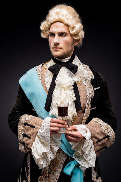 handsome victorian man in wig holding wine glass on black  - Foto, afbeelding