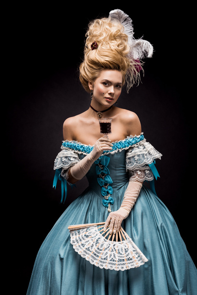 young victorian woman holding wine glass and fan on black  - Фото, изображение