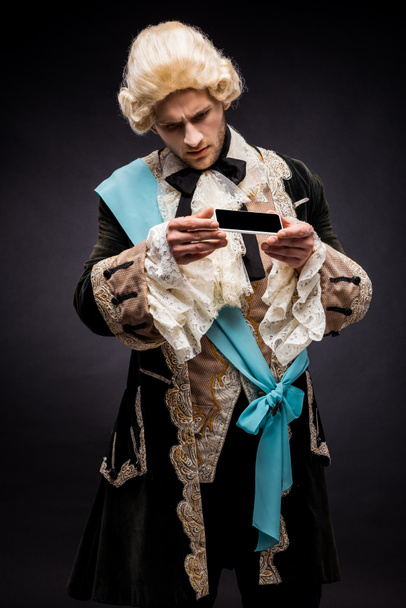 handsome victorian man in wig looking at smartphone with blank screen on black  - Photo, Image