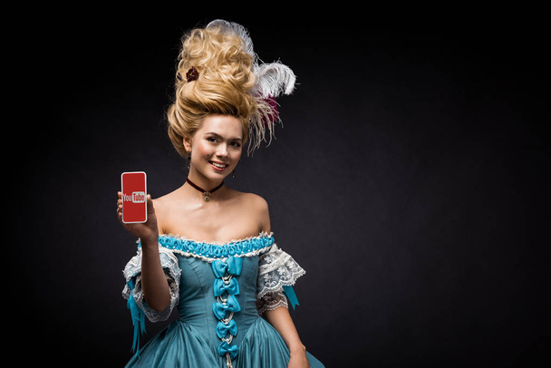 KYIV, UKRAINE - JUNE 5, 2019: attractive victorian woman holding smartphone with youtube app on screen on black  - Photo, Image
