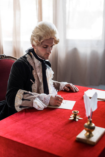 selective focus of handsome victorian man in wig holding feathers and writing letter  - Photo, Image