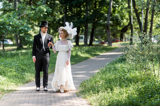 外を歩いている間に手をつないで帽子をかぶったハンサムなビクトリア朝の男と魅力的な女性  - 写真・画像