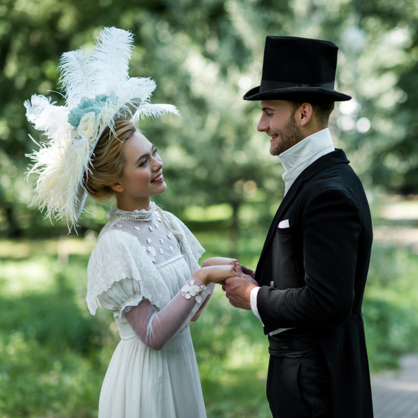alegre victoriano hombre y mujer en sombreros tomados de la mano mientras que de pie fuera
  - Foto, Imagen