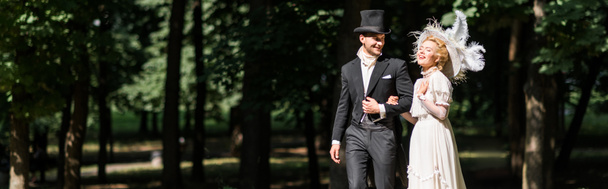 panoramic shot of happy young victorian woman and handsome man in hat walking outside  - Photo, Image