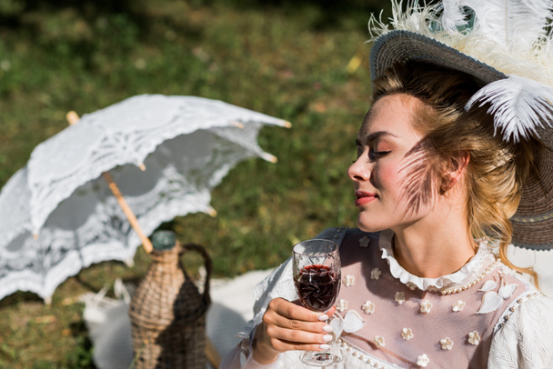 ワイングラスを持つ目を閉じた魅力的な若いビクトリア朝の女性の選択的な焦点  - 写真・画像