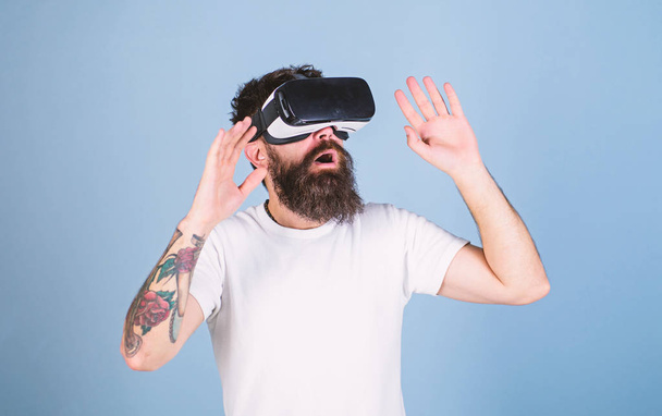 Man with beard in VR glasses, light blue background. VR gadget concept. Hipster on busy face exploring virtual reality with modern gadget. Guy with head mounted display interact in virtual reality - Photo, Image