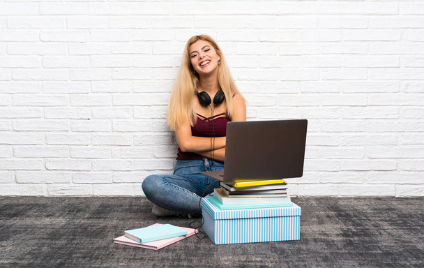 Teenager girl sitting on the floor with her laptop keeping the arms crossed in frontal position - Foto, Bild