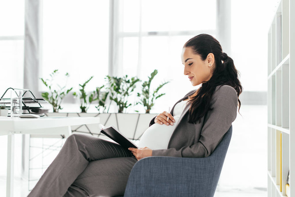 pregnant woman sitting in office in office chair and reading  - Photo, Image