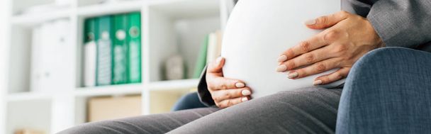 tiro panorámico de la mujer embarazada sosteniendo el vientre mientras está sentado en la silla de oficina
  - Foto, Imagen
