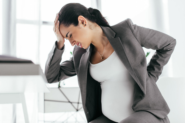 вагітна жінка тримає голову рукою через біль
  - Фото, зображення