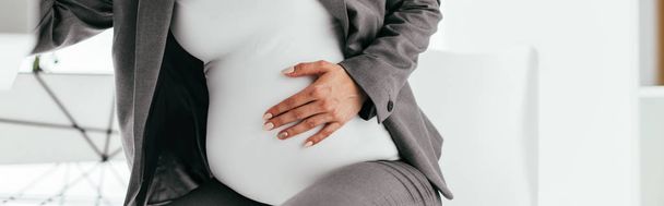 panoramic shot of pregnant woman holding her belly and sitting behind table - Foto, Imagen