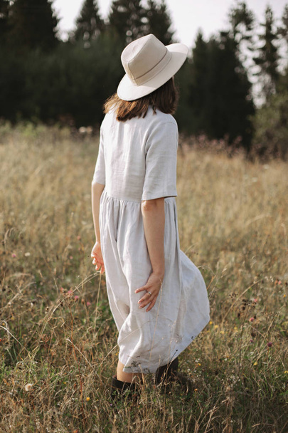Stylish girl in linen dress and hat walking among herbs and wild - Φωτογραφία, εικόνα