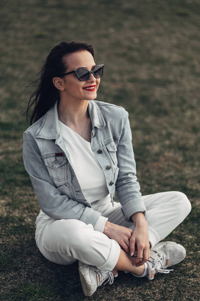 Hermosa chica morena en gafas de sol pantalones blancos y Jeans chaqueta, lápiz labial rojo
 - Foto, Imagen