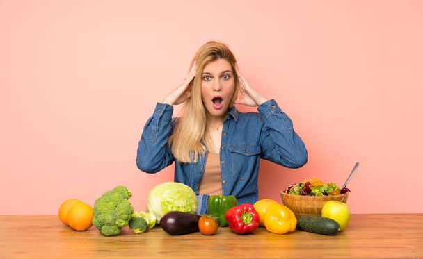 Mujer rubia joven con muchas verduras con expresión sorpresa
 - Foto, imagen