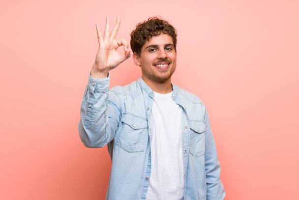 Homme blond sur un mur rose montrant un signe ok avec des doigts
 - Photo, image