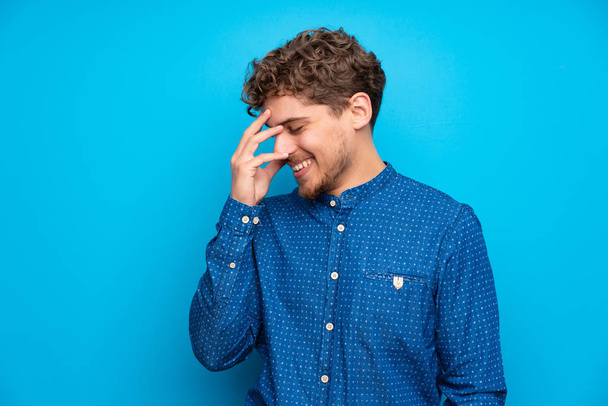 Ξανθιά άνδρα πάνω σε μια απομονωμένη μπλε τοίχο γελώντας - Φωτογραφία, εικόνα