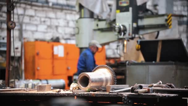 In de fabriek op de tafel zijn metalen onderdelen en gereedschappen-op de achtergrond, een man werkt op een machine tool - Video