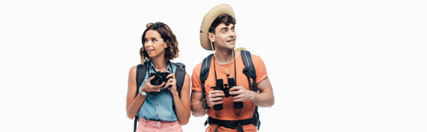 panoramic shot of two smiling tourists with digital camera and binoculars looking away isolated on white - Foto, Imagem