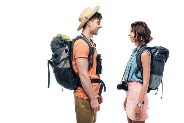 two young, smiling tourists with backpacks looking at each other isolated on white - 写真・画像