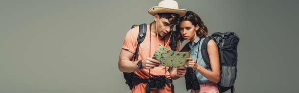 panoraamakuva kahdesta nuoresta matkailijasta katselemassa maantieteellistä karttaa harmaalla pohjalla
 - Valokuva, kuva