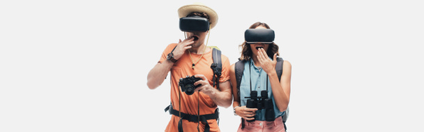 panoramic shot of two surprised tourists using virtual reality headsets isolated on grey - Photo, Image
