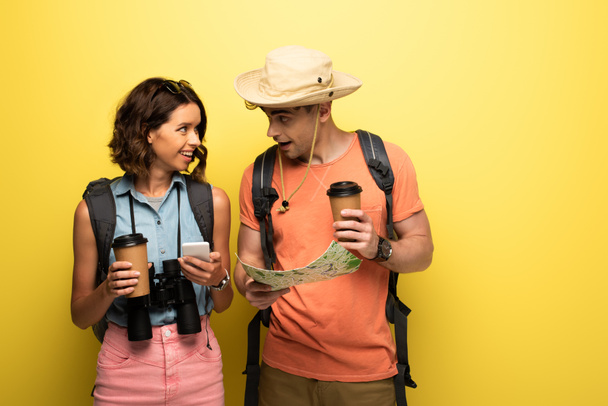 souriant jeune femme tenant smartphone tout en regardant l'homme avec carte géographique sur fond jaune
 - Photo, image