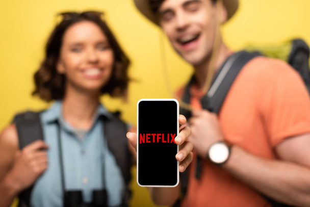 KYIV, UKRAINE - JUNE 3, 2019: Selective focus of smiling woman showing smartphone with Netflix app while standing near cheerful man on yellow background. - Foto, Imagem