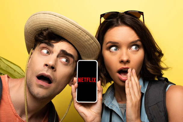 KYIV, UKRAINE - JUNE 3, 2019: Shocked young woman showing smartphone with Netflix app while standing near surprised man on yellow background. - 写真・画像