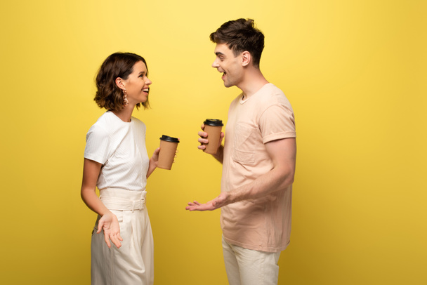 mosolygós férfi és nő beszél, miközben papír csésze sárga háttérrel - Fotó, kép