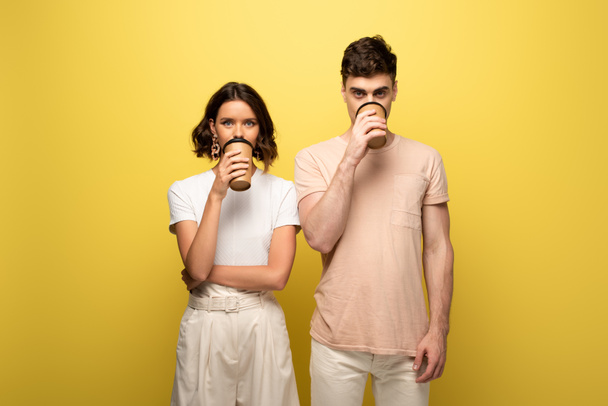 young man and woman drinking coffee to go while drinking coffee to go on yellow background - Foto, Imagem