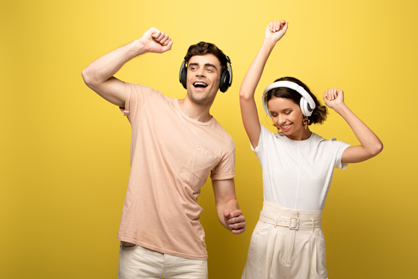 happy young man and woman dancing while listening music with headphones on yellow background - Fotoğraf, Görsel