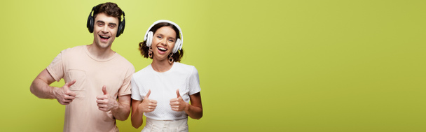 panoramic shot of excited man and woman smiling at camera and showing thumbs up on green background - Fotó, kép