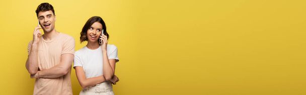 panoramic shot of young man and woman talking on smartphones on yellow background - Fotó, kép