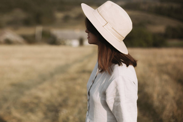Stylish girl in linen dress and hat walking in sunny field grass - Foto, Imagem