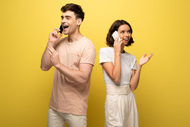 smiling man and woman talking on smartphones and looking away on yellow background - Fotó, kép