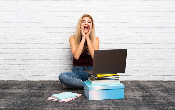 Menina adolescente sentada no chão com seu laptop gritando e anunciando algo
 - Foto, Imagem