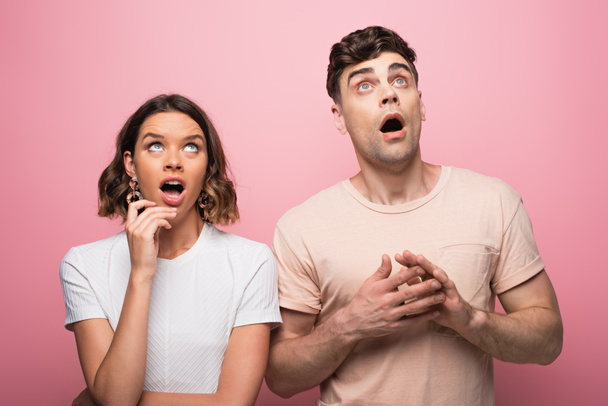 shocked man and wooman looking up and gesturing on pink background - Fotoğraf, Görsel