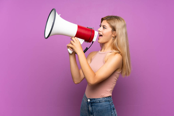 Adolescente chica sobre aislado púrpura fondo gritando a través de un megáfono
 - Foto, Imagen
