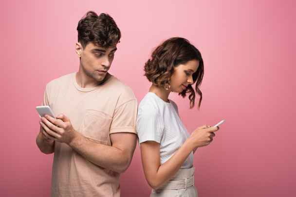 young man and woman using smartphones on pink background - Fotografie, Obrázek