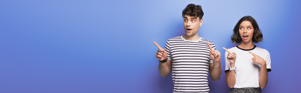 panoramic shot of positive man and woman looking away and pointing with fingers on blue background - Photo, Image
