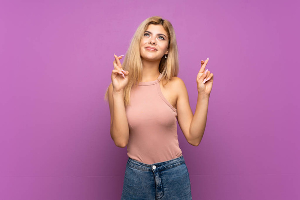 Teenager girl over isolated purple background with fingers crossing and wishing the best - Photo, Image