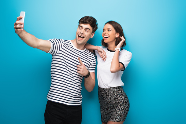 cheerful man taking selfie with attractive, smiling girl on blue background - Foto, Imagen