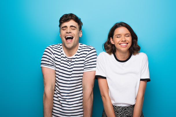 excited man and woman laughing with closed eyes on blue background - 写真・画像