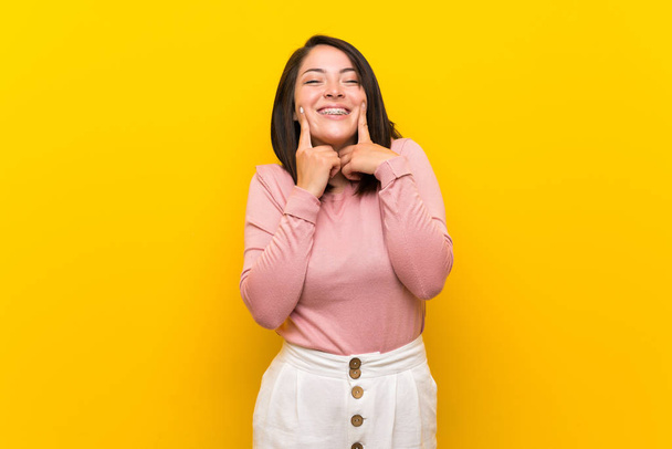 Νεαρή Μεξικάνα γυναίκα πάνω από απομονωμένο κίτρινο φόντο χαμογελώντας με μια ευτυχισμένη και ευχάριστη έκφραση - Φωτογραφία, εικόνα