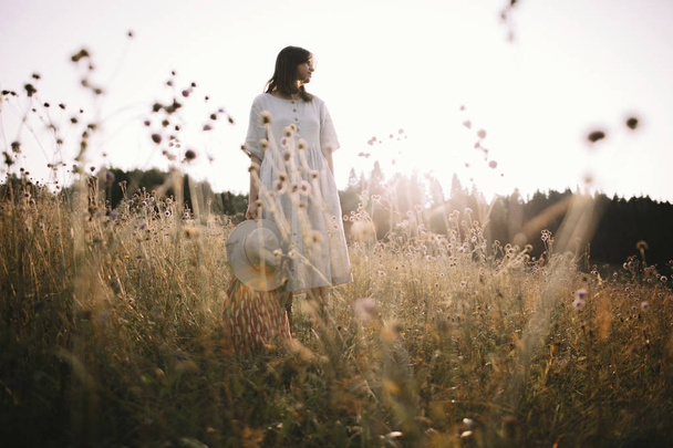 Stylish girl in rustic dress standing among wildflowers and herb - Photo, Image