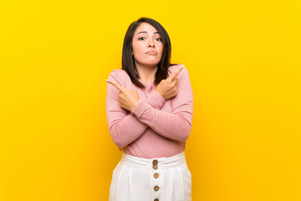 Giovane donna messicana su sfondo giallo isolato che punta ai laterali avendo dubbi
 - Foto, immagini